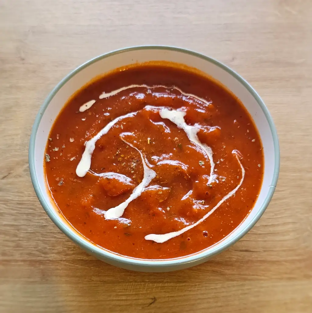 A bowl of Italian style tomato soup with cream dressing in a bowl on a wooden table